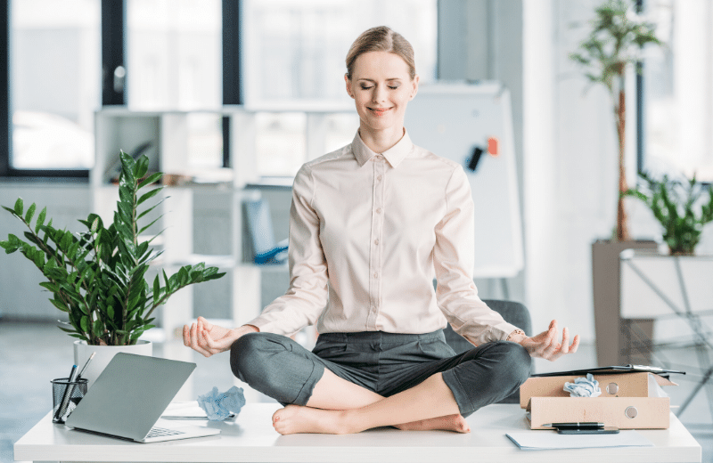 mujer sentanda encima de mesa de escritorio haciendo meditacion | Teletrabajo